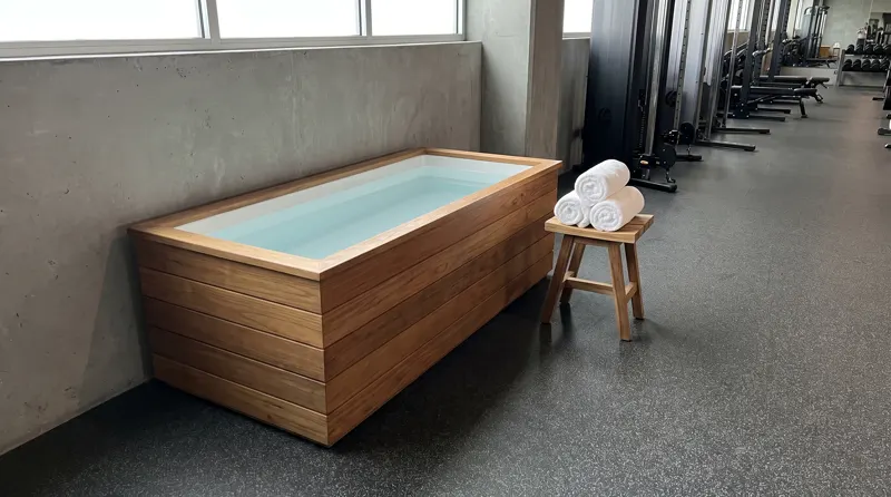 Bak cold plunge jati dengan handuk di sudut gym modern