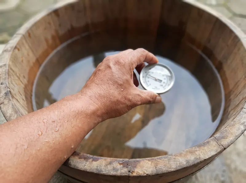 Tangan memegang termometer apung di atas air bak jati